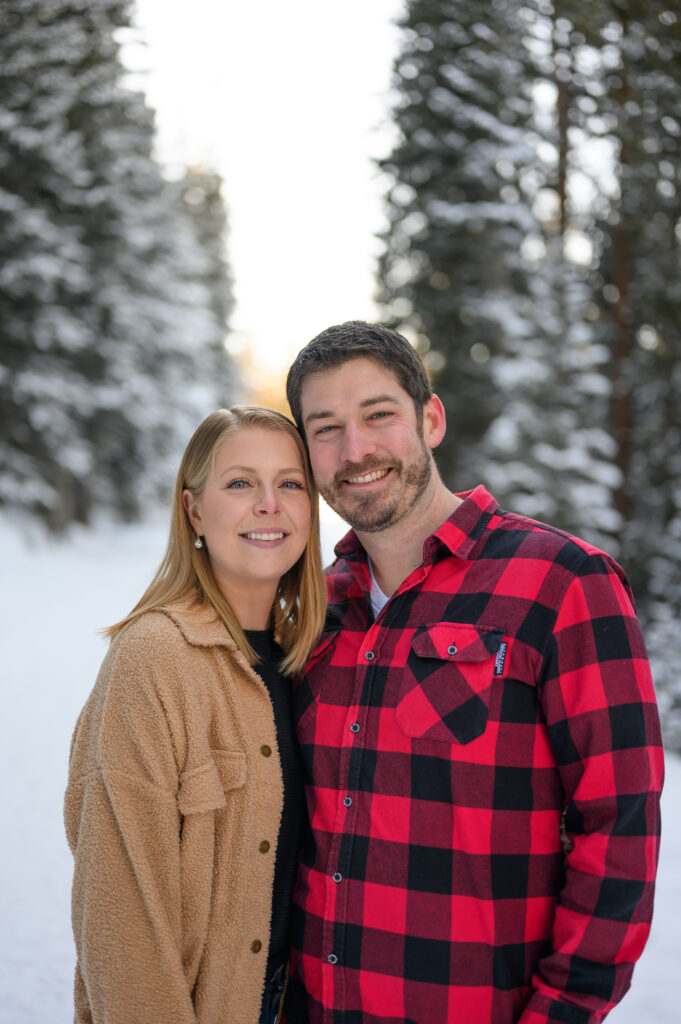 Couple smiling on snowy pathway with trees